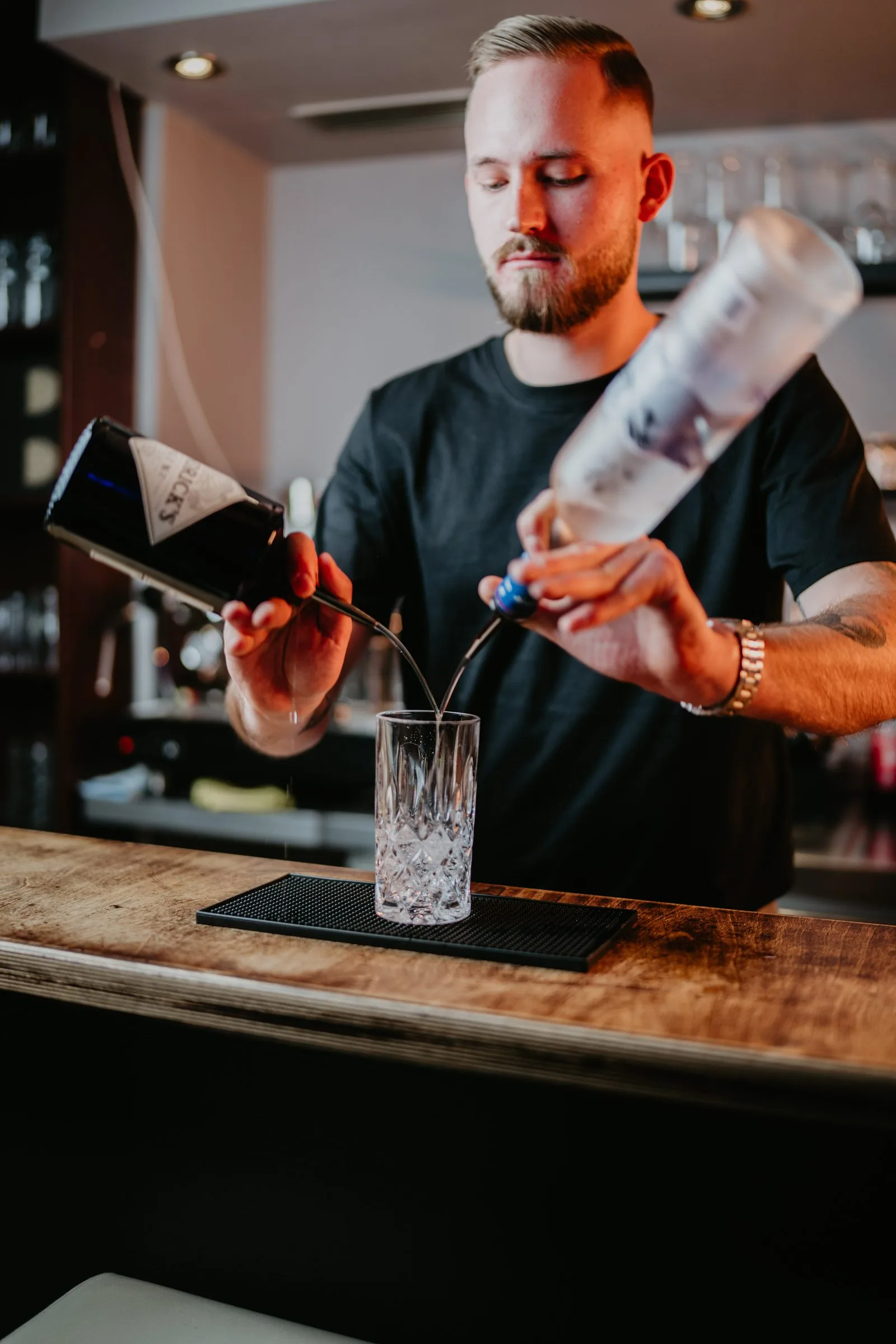 Ein Barkeeper gießt aus zwei Flaschen gleichzeitig in ein Glas.