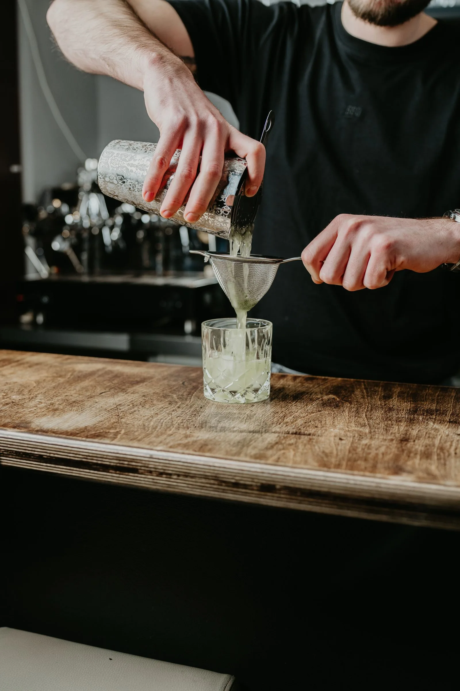 Ein Cocktail wird aus dem Shaker durch ein Sieb ins Glas abgeseiht.