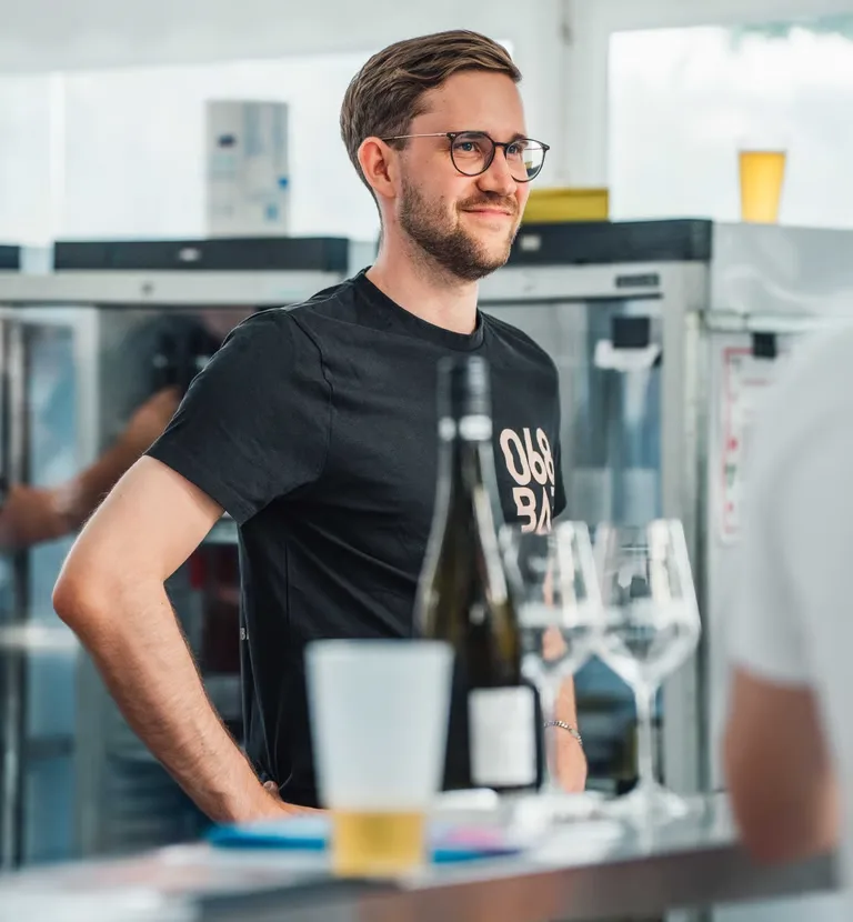 Ein Mitarbeiter der 068 steht hinter der mobilen Bar, davor Weinflasche, Gläser und ein Bier.