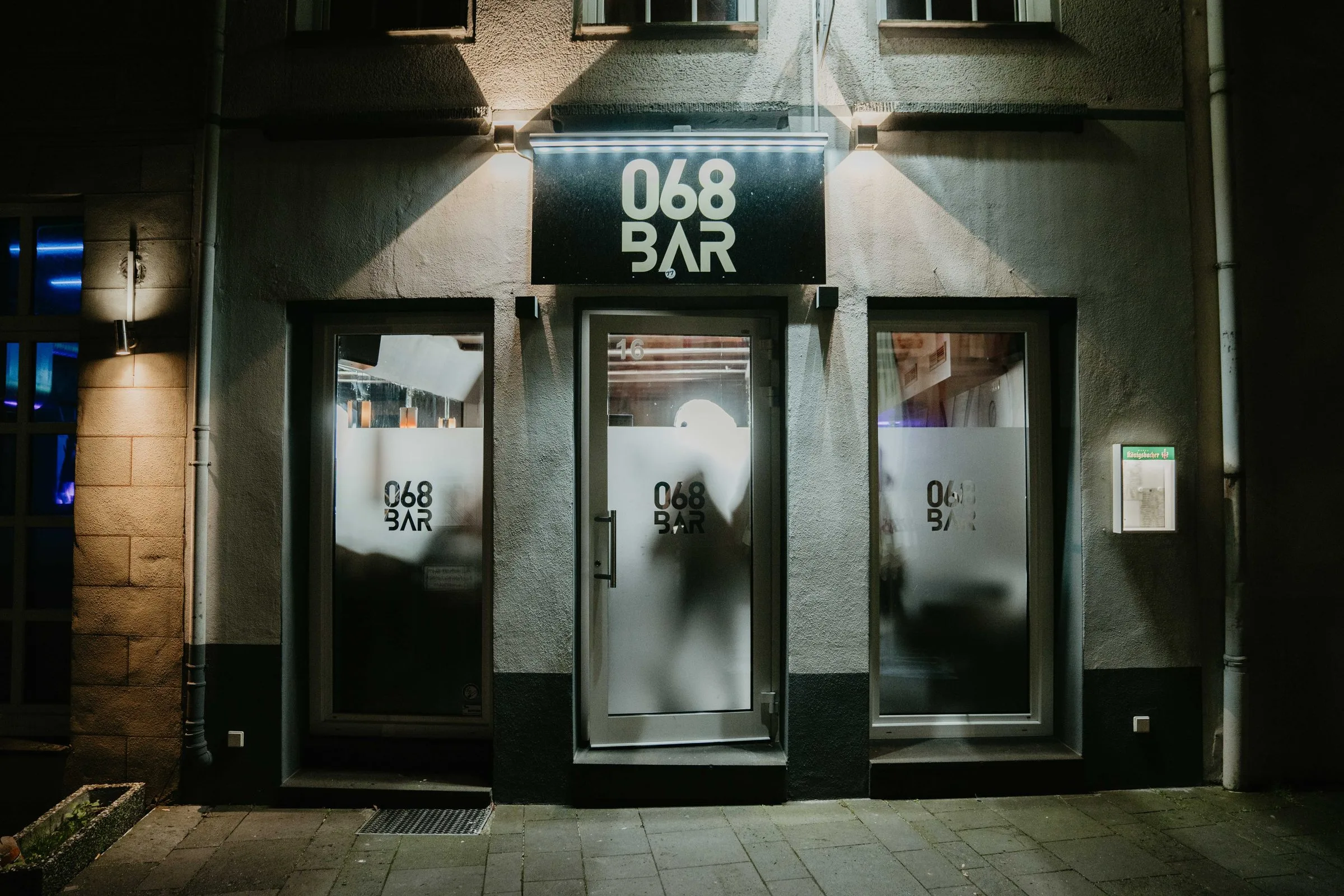 Der beleuchtete Eingang der 068 Bar mit Logo über der Tür bei Nacht.