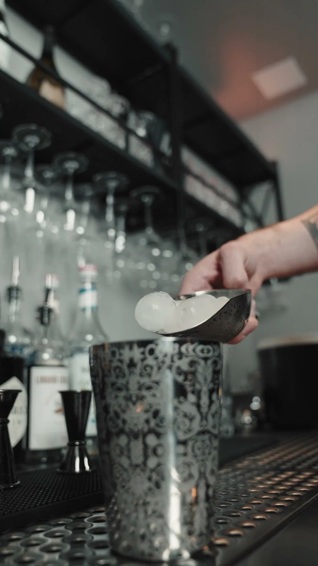 Ein Barkeeper füllt Eis in den Shaker, darüber hängen Gläser.