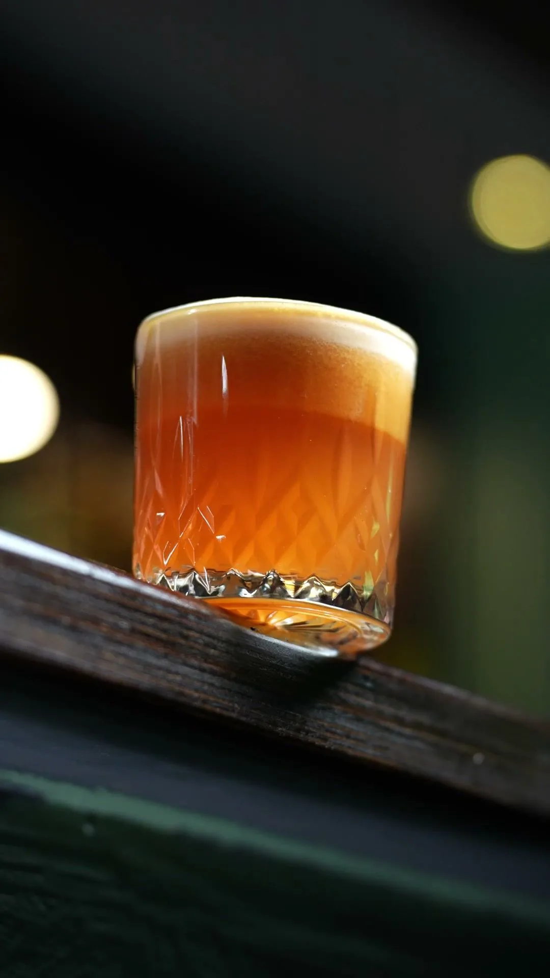 Ein Cocktail steht auf der Kante des Tresens, dahinter warme Lichter.