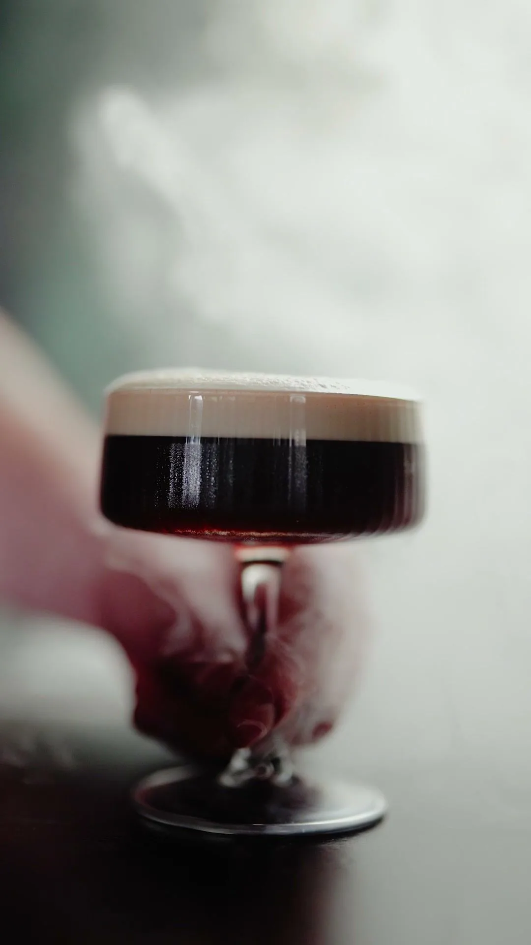 Ein Espresso Martini im Stielglas vor hellem Rauch.
