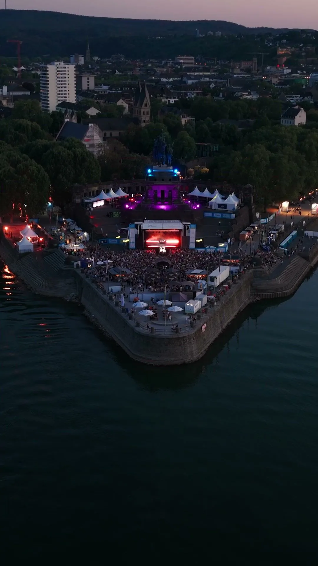 Luftaufnahme eines Festivals am Rheinufer in der Abenddämmerung.