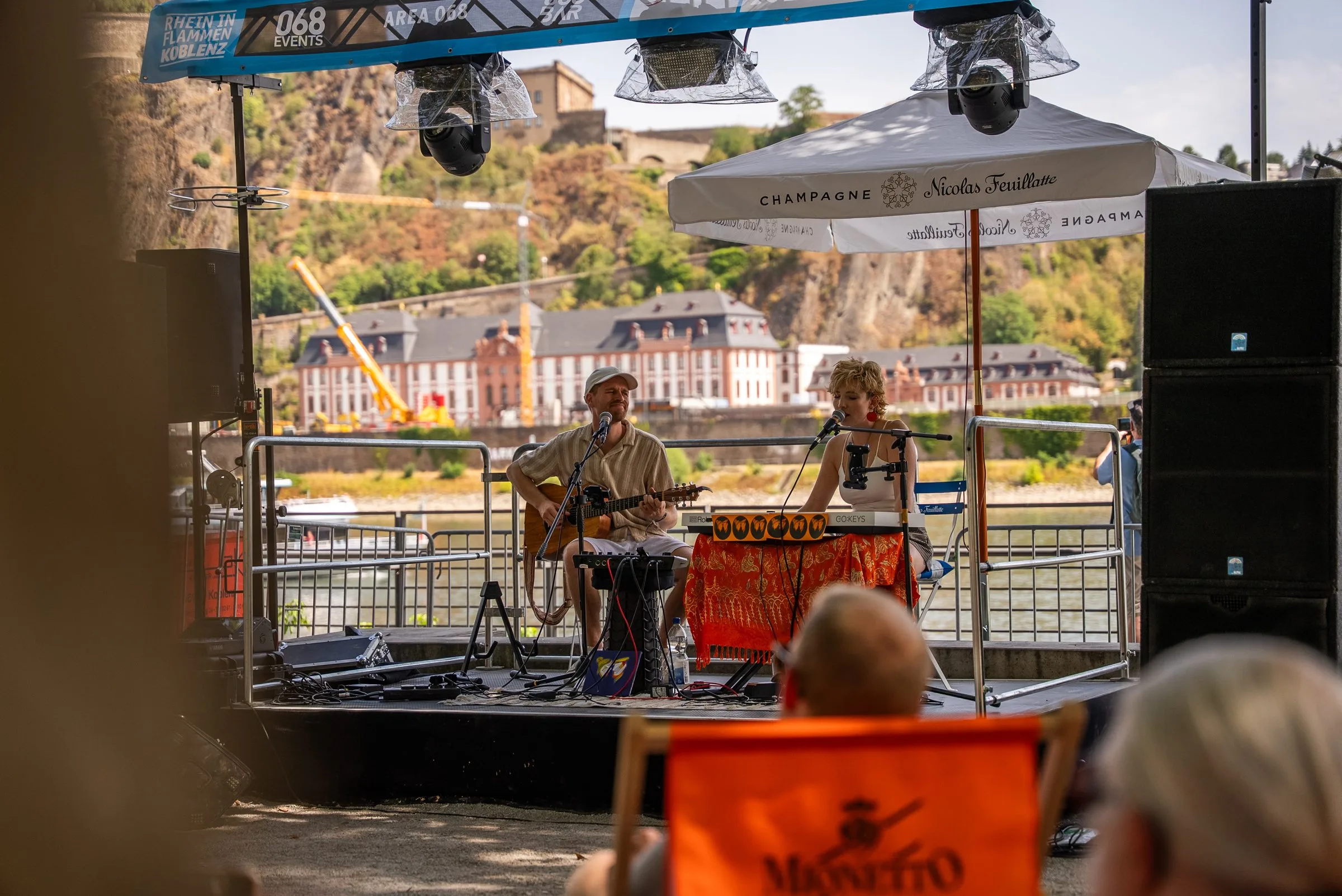 Ein Akustik-Duo spielt auf der 068-Events-Bühne am Rhein, im Hintergrund die Festung Ehrenbreitstein.