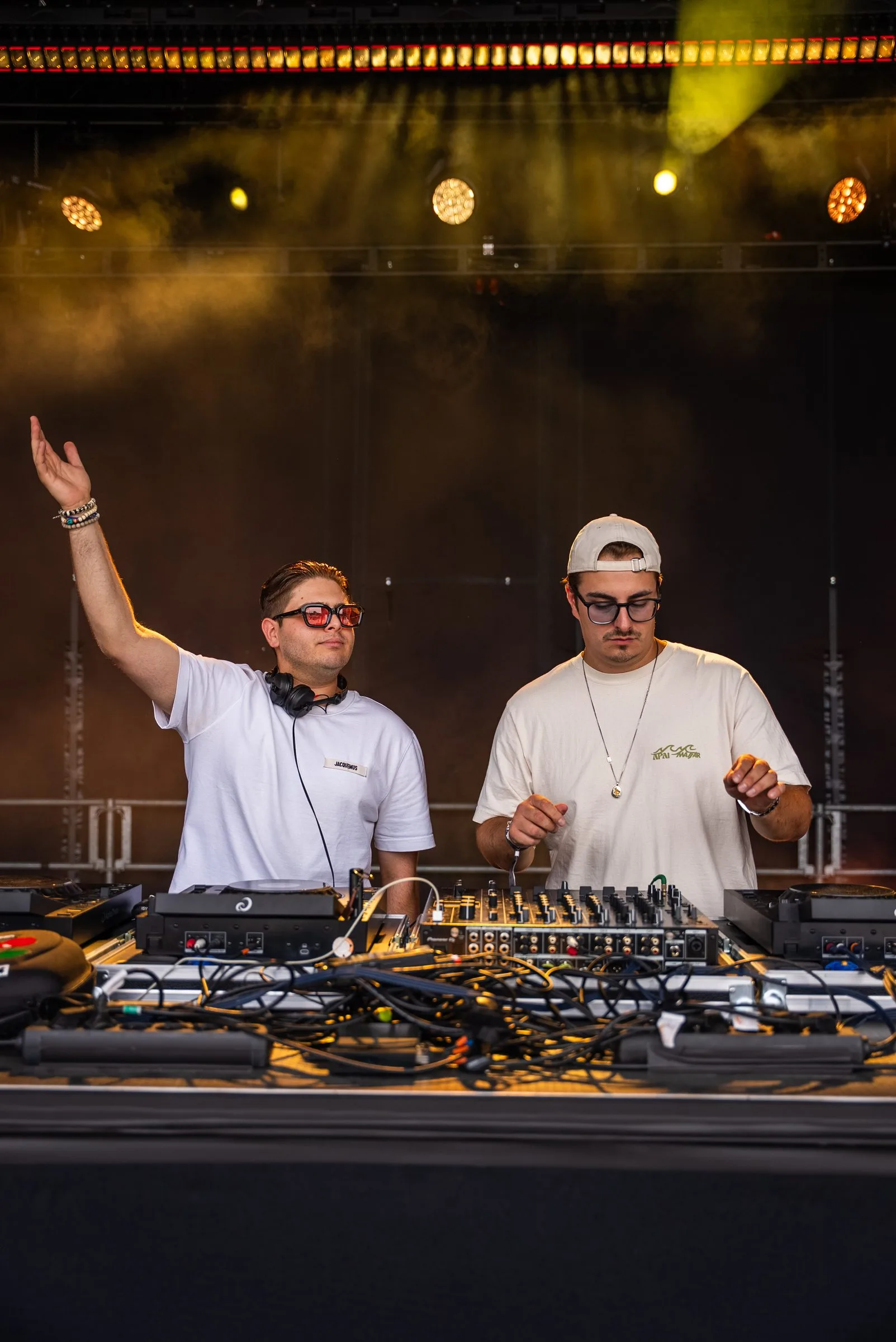 Zwei DJs in weißen Shirts auf der Bühne, einer reißt den Arm hoch.