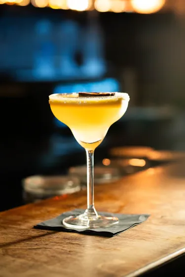Ein gelber Cocktail im Stielglas mit einer dekorativen Schaumkrone.