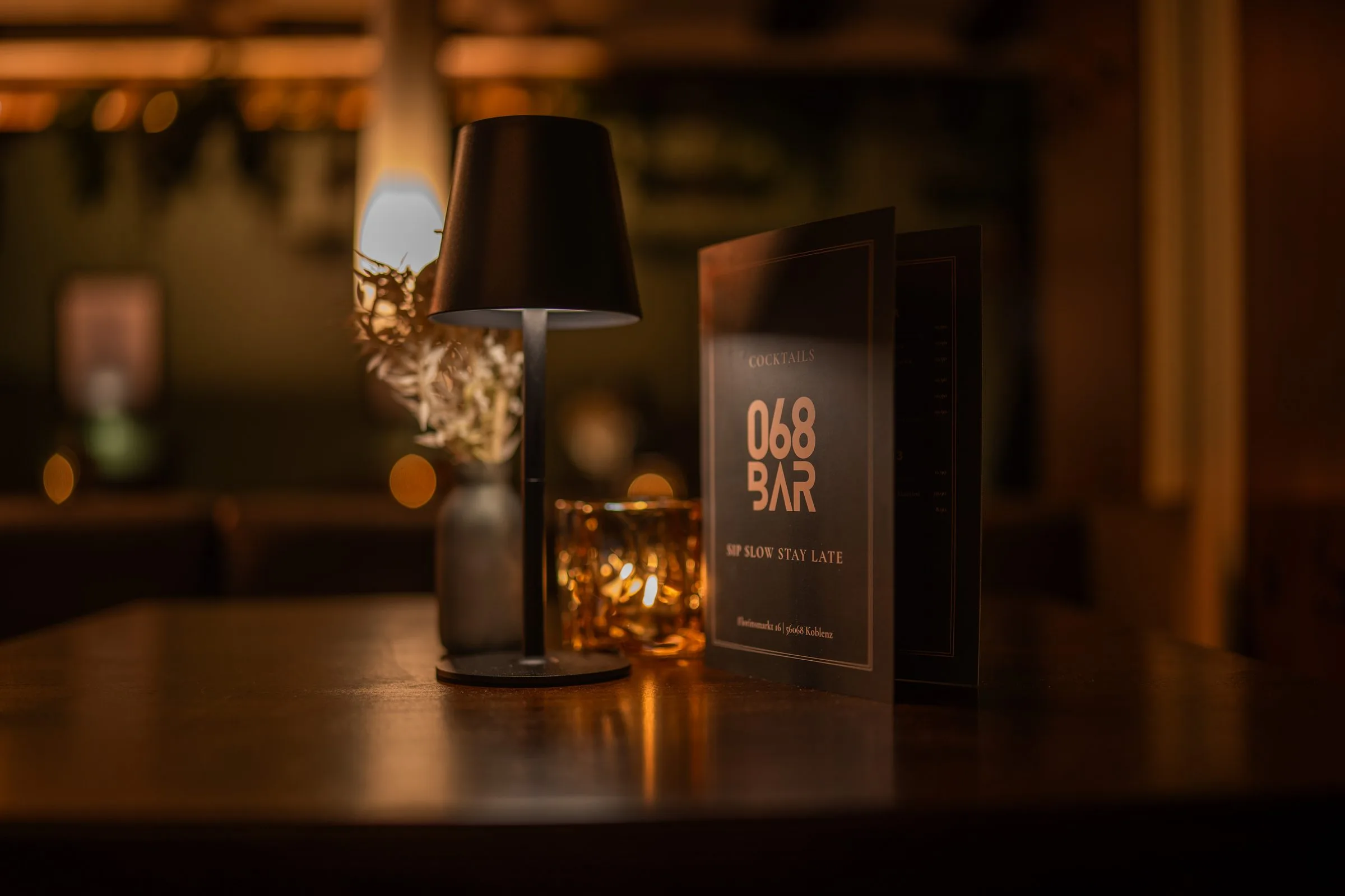 Ein Tisch in warmem Licht mit Tischlampe, Windlicht und der Karte der 068.